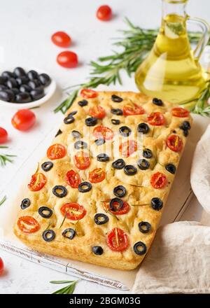 Focaccia mit Tomaten, Oliven und Rosmarin, vertikal. Ganze italienische Fladenbrot, Flasche mit Öl Stockfoto