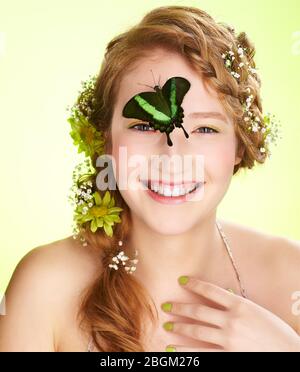 Ausdruck Porträt von schönen gesunden lächelnden Rotschopf jugendlich Mädchen mit Blumen in ihrem Haar halten Schmetterling auf ihrem Gesicht Stockfoto