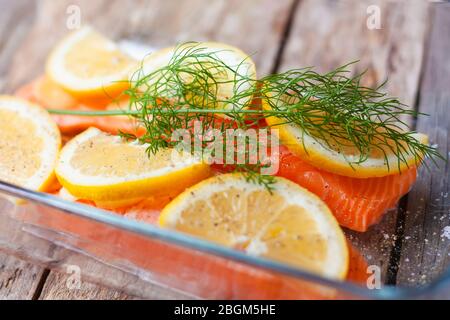 Roter Fisch oder Lachsfilets in.Glas Backform auf Holzhintergrund. Frischer Fisch, Zitrone und Dill zum Kochen von Zutaten. Stockfoto