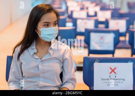 Junge asiatische Touristen Frau mit Maske und sitzen mit Abstand am Flughafen Stockfoto