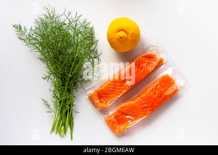 Roter Fisch oder Lachsfilets in Vakuumverpackung auf weißem Hintergrund. Frische Fisch-, Zitronen- und Dill-Kochzutaten. Omega-3 Stockfoto