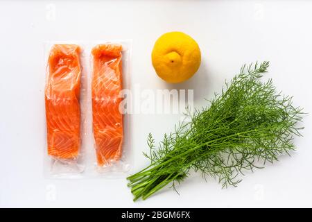 Roter Fisch oder Lachsfilets in Vakuumverpackung auf weißem Hintergrund. Frische Fisch-, Zitronen- und Dill-Kochzutaten. Omega-3 Stockfoto