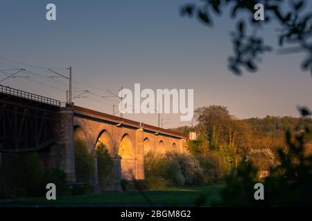 Eisenbahnbrücke von Mariaort mit Steinbögen und Oberleitung über Grünfeld, die am späten Nachmittag in der Sonne in Regensburg, Bava glüht Stockfoto