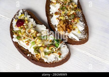 Gesundes makrobiotisches Frühstück. Sandwich mit Frischkäse, Erbsen-Mikrogreens und gekeimten Mungbohnen, Walnuss, Sonnenblume und Flachs auf Holzhintergrund. Stockfoto