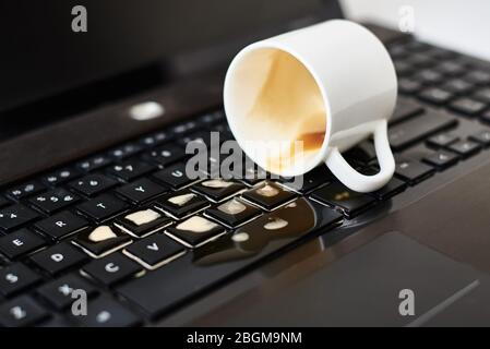 Verschütten Sie Kaffee aus der weißen Tasse auf der Laptop-Tastatur des Computers.Beschädigung des Computers durch verschüttete Flüssigkeit Stockfoto