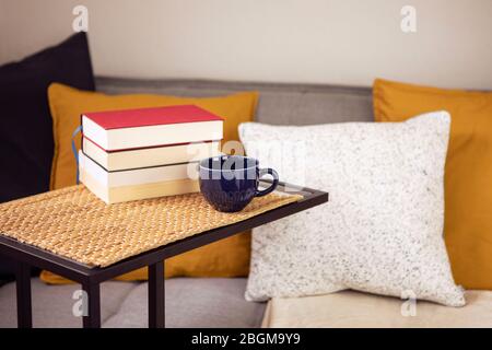 Interieur mit Büchern auf dem Tisch, Tasse Kaffee oder Tee mit gemütlichen Sofa mit Kissen und Kissen. Bücher zu Hause lesen, lernen. Freizeitaktivitäten Stockfoto