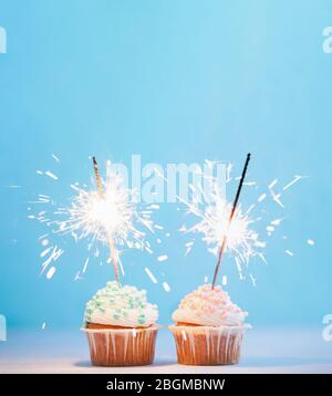 Zwei Cupcakes mit bunten Streuseln und Glitzern dekoriert. Festliche Cupcakes mit blauen und rosa Streuseln auf blauem Hintergrund mit Copy Space Top für Text oder Design Stockfoto