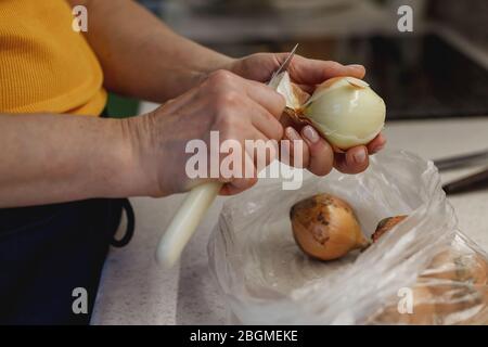 Die Hände der Frau schälen frische Zwiebel über einer kleinen Plastiktüte Stockfoto