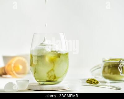 Iced Matcha Latte Tee mit Schlagsahne aus Tumbler Glas und Zutaten auf weißem Marmor Hintergrund. Kopierbereich für txt oder Design Stockfoto