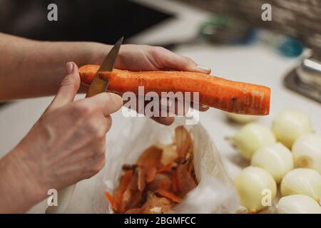 Die Hände der Frau schälen gerade frische Karotte über einer kleinen Plastiktüte Stockfoto