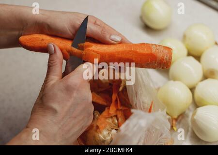 Die Hände der Frau schälen gerade frische Karotte über einer kleinen Plastiktüte Stockfoto