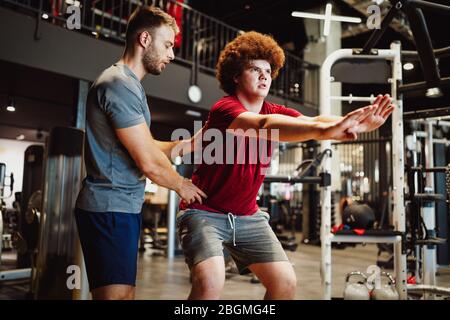 Übergewichtiger junger Mann trainiert mit persönlichem Trainer die Sporthalle Stockfoto