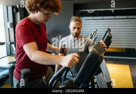 Übergewichtiger junger Mann trainiert mit persönlichem Trainer die Sporthalle Stockfoto