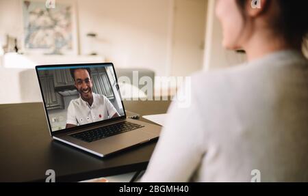 Frau sitzt am Tisch mit Videoanruf mit ihrem Mann auf dem Laptop. Ein Paar trifft sich per Videoanruf auf einem Laptop. Blick von hinten. Stockfoto