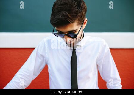 Ein lächelnder Mann in formaler Kleidung und Sonnenbrille steht draußen. Geschäftsmann in weiß und schwarz, der draußen lächelt. Stockfoto