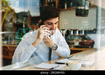 Geschäftsmann, der telefoniert, während er in einem Café arbeitet. Ein Mann, der seine Arbeit macht, sitzt in einem Café. Stockfoto