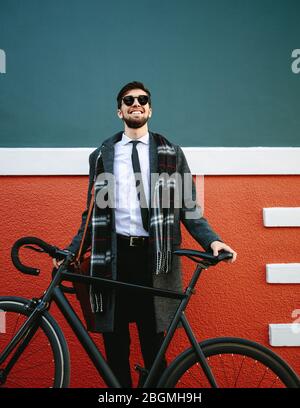 Lächelnder Mann, der mit dem Fahrrad zur Arbeit geht. Geschäftsmann steht an seinem Fahrrad auf Bürgersteig im Freien. Stockfoto