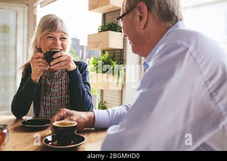 Älteres Paar sitzt am Tisch und trinkt Kaffee im Café. Fröhliches älteres Paar, das sich unterhält und eine Tasse Kaffee im Café genießt. Stockfoto