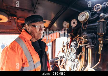 Ein Mann macht eine Pause, während er sich im Fahrerhaus lehnt, mit Messingzifferblättern und Kupferrohren im Hintergrund arbeitet britische Dampflokomotive, die Sir nig Stockfoto