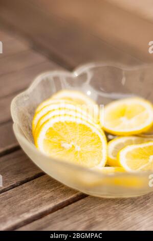 Eine mit Zitronenkeilen gefüllte Glasschale steht auf einem Holztisch. Mit dem Löffel werden die Scheiben in erfrischendes Wasser oder Limonade gegeben. Stockfoto