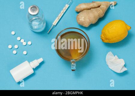 Nasenspray, Pillen, eine Glasflasche, ein Quecksilberthermometer, eine Tasse Tee, Zitrone und Ingwer. Draufsicht. Konzept des Behandlungskits. Gesundheit Heilmittel Lebensmittel für col Stockfoto