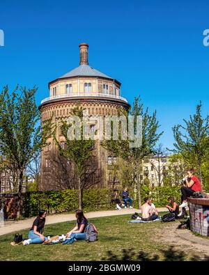 Während der COVID-19 Pandemie sitzen die Menschen in der Sonne und halten eine sichere soziale Distanz. Im Wasserturm Park, Kollwitzplatz, Berlin. Stockfoto