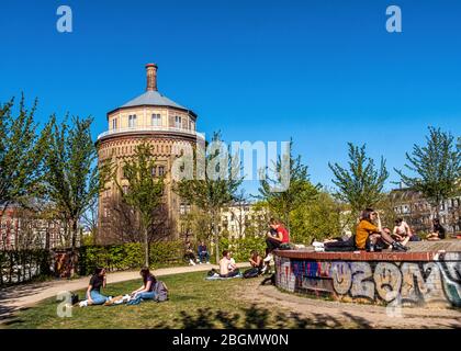 Während der COVID-19 Pandemie sitzen die Menschen in der Sonne und halten eine sichere soziale Distanz. Im Wasserturm Park, Kollwitzplatz, Berlin. Stockfoto