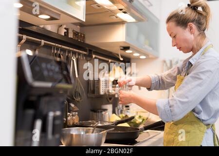 Wohnen Sie zu Hause Hausfrau Frau, die in der Küche kocht, in einem Topf salzt und Essen für das Familienessen zubereitet. Stockfoto