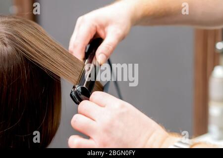 Friseurhände sind Glätten Haar der Frau mit Haarglätter Werkzeug im Friseursalon, Rückansicht. Stockfoto