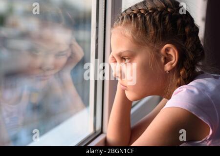 Müde von Selbstisolierung, schaut ein gelangweiltes Quarantänemädchen aus dem Fenster Stockfoto