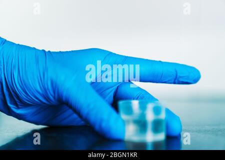 Hand mit einem blauen Latexhandschuh, der einen Messbecher voll Desinfektionsmittel hält. Stockfoto