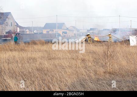 Feuerwehrleute in der Feuerwehr Ausrüstung Kampf Feuer trockenes Gras im Frühjahr. Asov deutscher Nationalbezirk der Region Omsk, Russland, 18.04.2020. Stockfoto