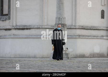 Bukarest, Rumänien - 18. April 2020: Ein orthodoxer christlicher Priester mit einer chirurgischen Maske wegen der COVID-19 Pandemie trägt das Heilige Licht während der Stockfoto