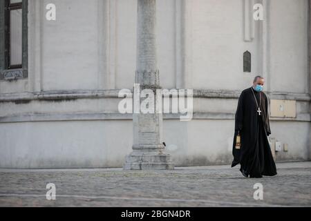 Bukarest, Rumänien - 18. April 2020: Ein orthodoxer christlicher Priester mit einer chirurgischen Maske wegen der COVID-19 Pandemie trägt das Heilige Licht während der Stockfoto