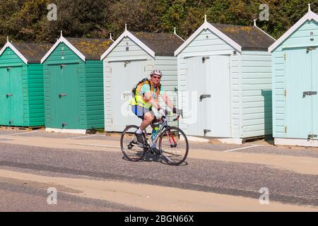 Bournemouth, Dorset, Großbritannien. April 2020. UK Wetter: Schöner warmer sonniger Tag, da die Temperaturen an den Stränden von Bournemouth an der Südküste steigen, während die Menschen ihre erlaubte Bewegung machen, die meisten halten sich an die Coronavirus Richtlinien. Mann Radfahrer Radfahren entlang der Promenade vorbei an Strandhütten - Fahrrad fahren. Quelle: Carolyn Jenkins/Alamy Live News Stockfoto