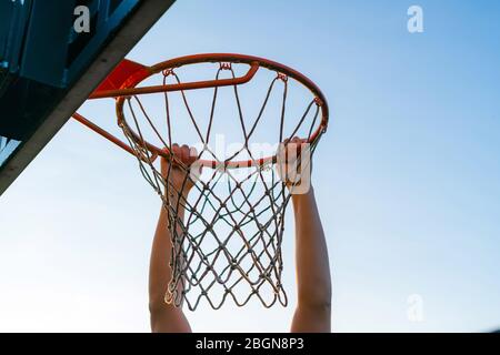 Street Basketball Slam Dunk Wettbewerb. Nahaufnahme des Spielers, der am Reifen hängt. Urban Jugend Spiel. Konzept des Erfolgs, Punkte sammeln und gewinnen Stockfoto