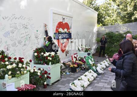 Mädchen schreibt Nachricht und die Menschen sehen Blumen auf Grenfell Jubiläum Stockfoto