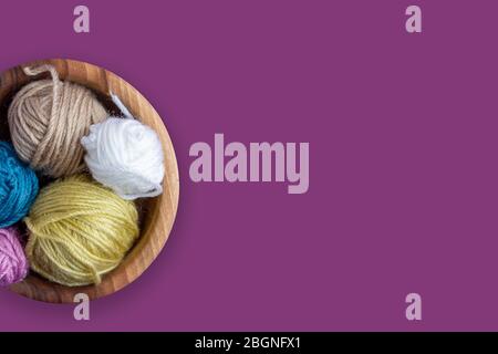 Lustige bunte Wollkugeln in Holzschale auf lila Hintergrund. Draufsicht. Stricken als Hobby. Kopierbereich. Hintergrund für Hobby-Shop. Stockfoto
