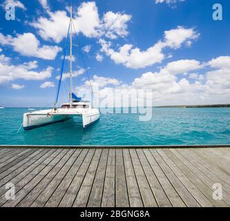 Leere Holzplattform mit Luxusyacht auf türkisfarbenem Wasser des Karibischen Meeres im Hintergrund, Dominikanische Republik verankert Stockfoto