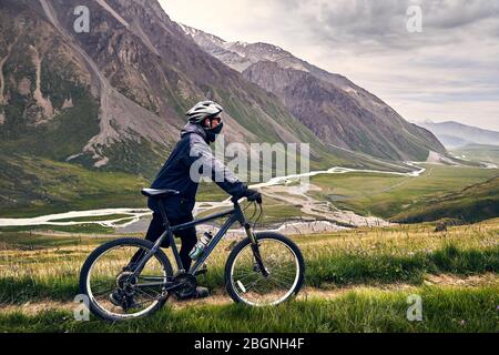 Mann auf Mountainbike Helm im Tal mit dem Fluss bei bewölktem Himmel Hintergrund. Stockfoto