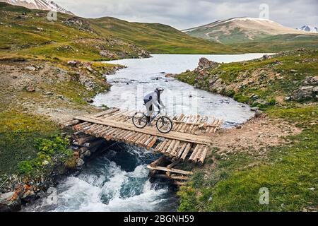 Mann auf dem Mountainbike den Fluss überqueren, die durch hölzerne Brücke im Tal Stockfoto