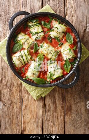 Mediterrane Zucchinibüllchen mit Ricotta und Kräutern in Tomatensauce in einer Pfanne auf einem Tisch Nahaufnahme gebacken. Vertikale Ansicht von oben Stockfoto