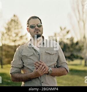 Junger modischer Mann mit Sonnenbrille im Freien. Analoges Filmporträt, aufgenommen im quadratischen Mittelformat. Stockfoto