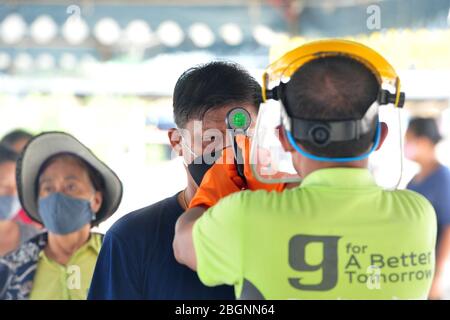 Bangkok, Thailand. April 2020. Ein Mann erhält Temperaturkontrolle an einem kostenlosen Lebensmittelverteilungspunkt in Bangkok, Thailand, 22. April 2020. Die thailändischen Behörden äußerten am Mittwoch Vertrauen in die jüngste Abwärtsentwicklung der COVID-19-Fallkurve, bei der 15 neue Fälle und ein Todesfall gemeldet wurden. Kredit: Rachen Sageamsak/Xinhua/Alamy Live News Stockfoto