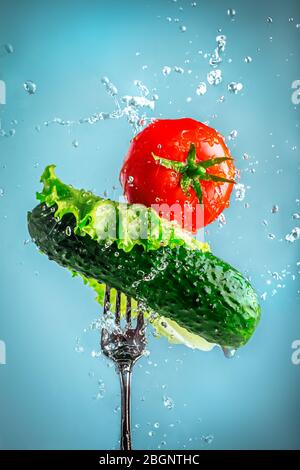 Gurke, Tomaten und Salat auf einer Gabel in Wasser spritzt auf blauem Hintergrund. Gemüse, natürliche, frische, gesunde, rohe Lebensmittel Stockfoto