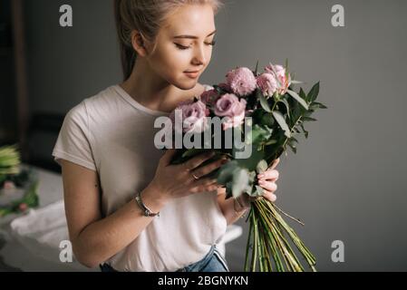 Nette blonde junge Frau, die Mode Kleidung schnuppert Bouquet von Blumen Stockfoto