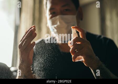 Coronavirus. Mann trägt in medizinischen Schutzmaske Reinigung Hände mit Desinfektionsmittel Spray im Haus, um Coronavirus, Covid-19, Grippe zu verhindern. Sprühflasche. Stockfoto