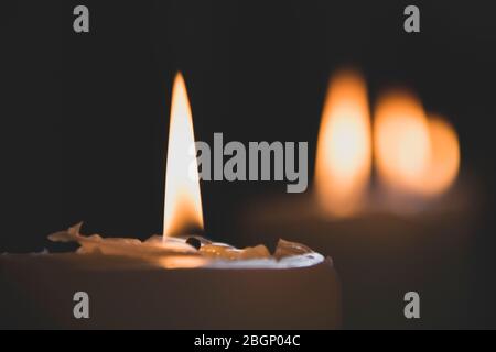 Nahaufnahme der klassischen Kerze mit orangen Flammen, die auf Wachs brennen, mit der Bokey anderer Kerzen in der Kirche Stockfoto