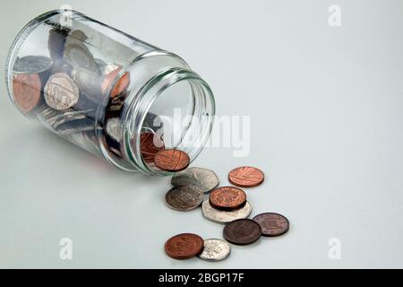 Glasflasche umgefallen, verschüttete Münzen auf weißen Tisch Stockfoto