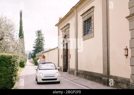 Schöne Braut, die in einem Cabrio vor der Medici Villa von Lilliano Wine Estate, Toskana, Italien steht. Stockfoto